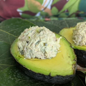 A bed of avocados leaves with a half of an avocado on it with tuna salad stuffed inside